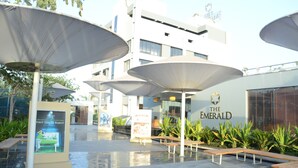 An outdoor seating area with umbrellas, benches, and a sign for 'The Emerald' hotel. - The Emerald Club (Lodhika)