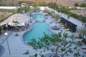 A large outdoor swimming pool with a bridge, surrounded by palm trees and lounge chairs. - The Emerald Club (Lodhika)