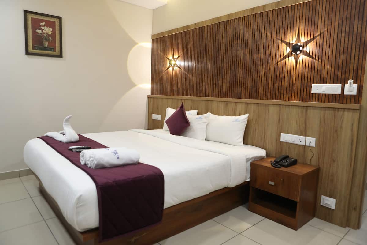 Ein Hotelzimmer mit einem hölzernen Kopfteil, einem Bett mit weißen Laken und einer violetten Decke, einem Nachttisch mit Telefon sowie einer wandmontierten Leuchte.