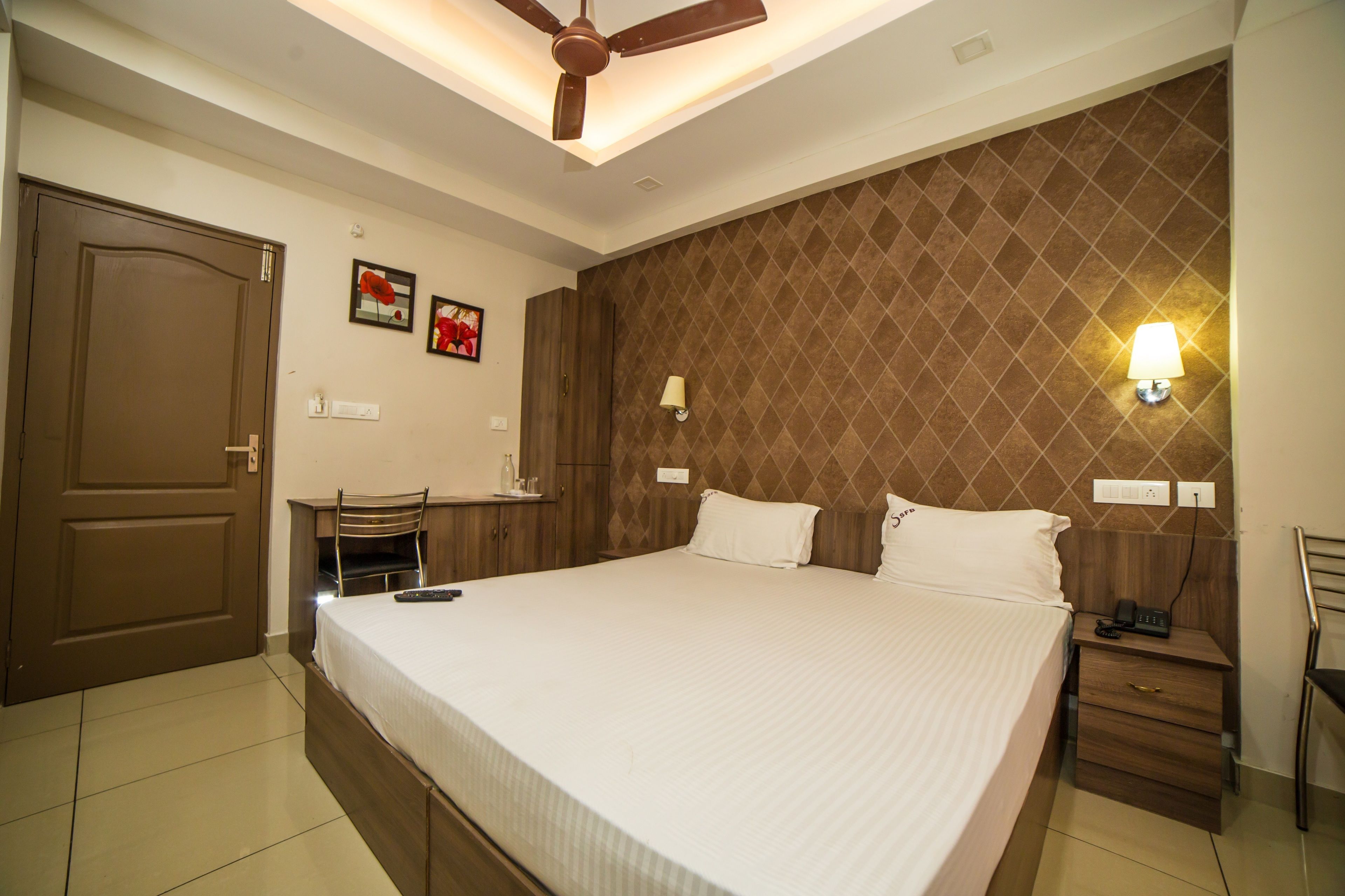 A bedroom with a large bed, a desk with a chair, a wardrobe, and a ceiling fan.