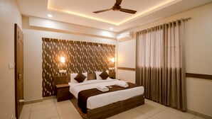 A hotel room with a large bed, a ceiling fan, a wall-mounted air conditioner, and a window with curtains. - Spring Field Billets (Kanayannur)