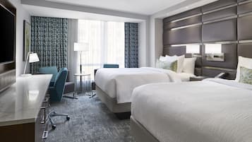 A hotel room with a large bed, a desk, a chair, a TV, and a window with curtains.