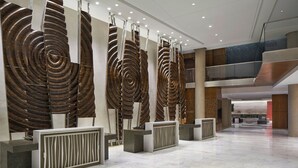 Una hall moderna con una reception, un'ampia opera d'arte a spirale sulla parete e un pavimento spazioso in marmo.