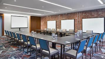A conference room with a long table, blue chairs, and a brick wall.