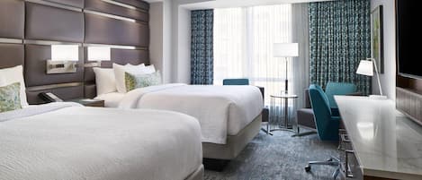 A hotel room with two beds, a desk, a chair, a TV, and a small table.