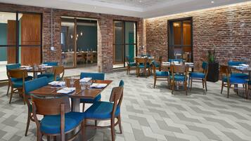 A modern dining area with brick walls, wooden tables, and blue upholstered chairs.