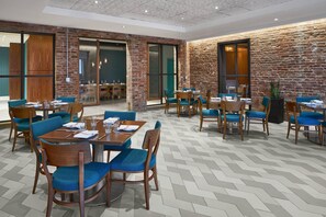 A modern dining area with brick walls, wooden tables, and blue upholstered chairs. - Courtyard by Marriott Washington Downtown/Convention Center (Washington)