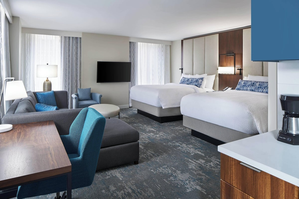 A hotel room with two beds, a sofa, a coffee table, and a TV.