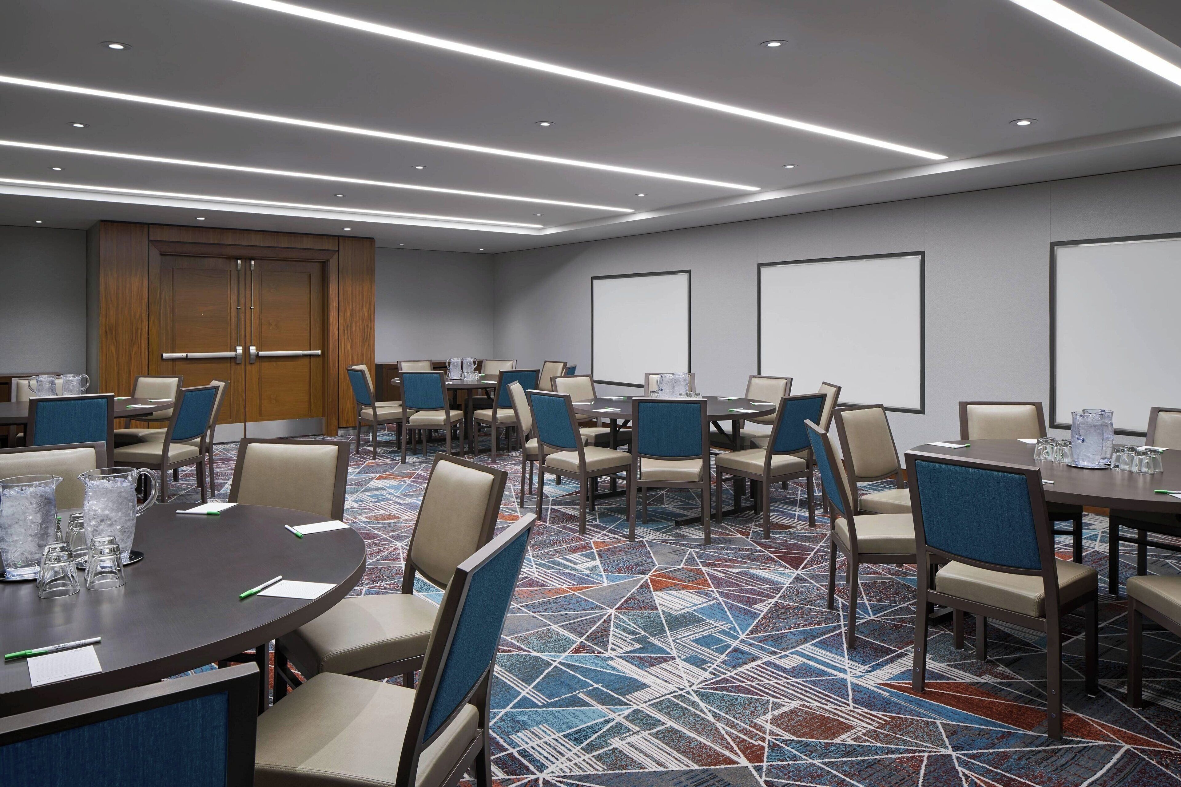 A conference room with multiple tables and chairs, equipped with water pitchers and glasses, and a patterned carpet.