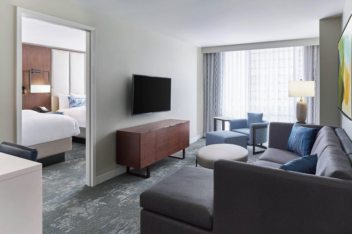A modern hotel room with a bed, a flat-screen TV, a sofa, a small table, and a lamp.