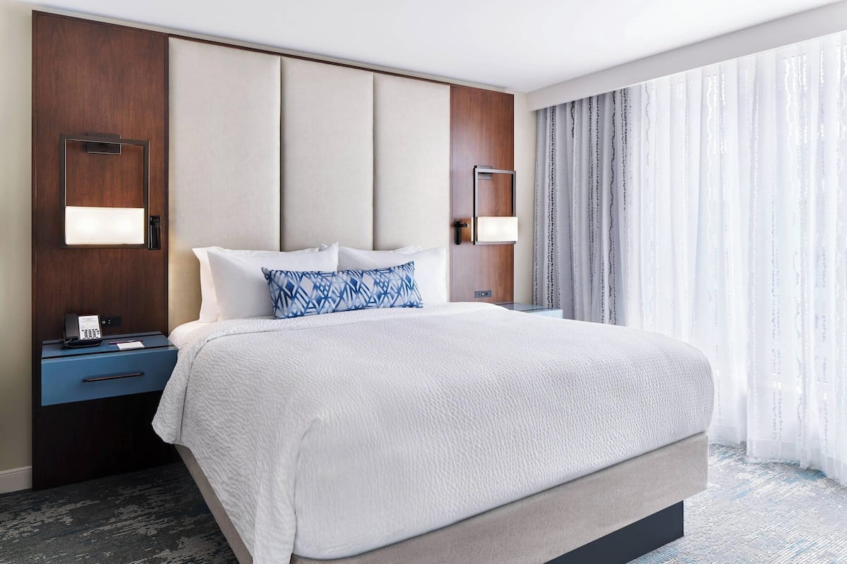 A hotel room with a large bed, a nightstand with a phone, and a window with curtains.