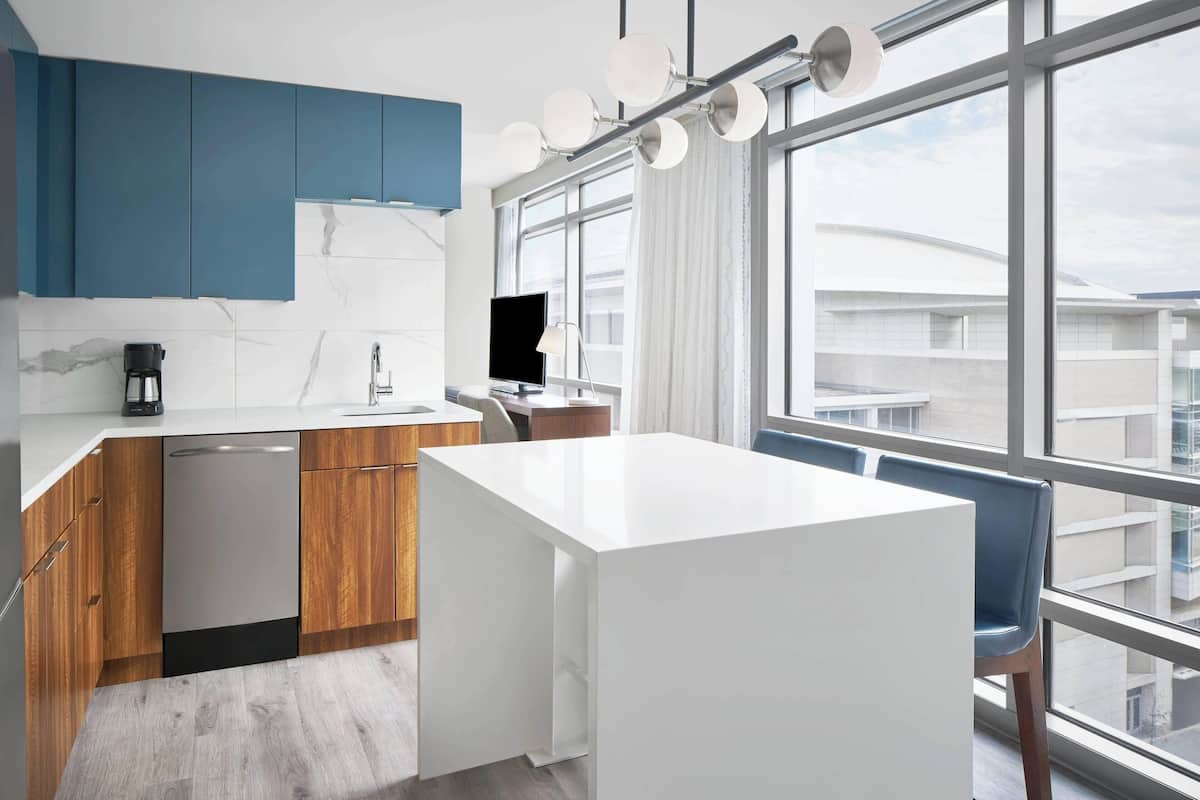 A modern kitchen with blue cabinets, a white countertop, and a large window offering a view of buildings.