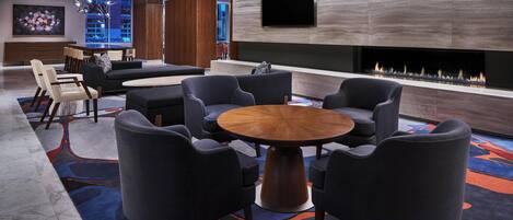 A modern lounge area with a round wooden table surrounded by chairs, a flat-screen TV mounted on the wall, and a built-in fireplace.