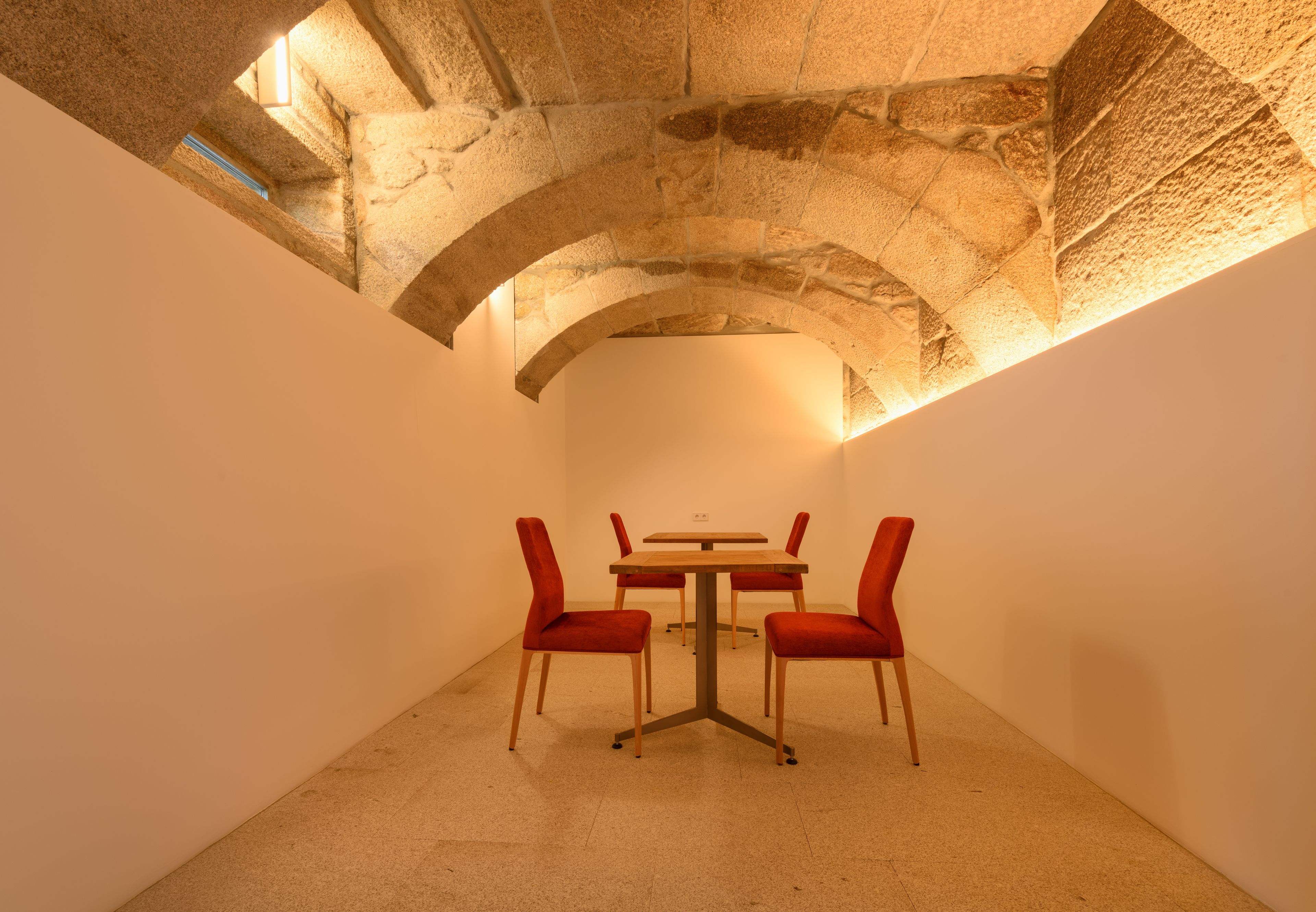 A dining area with a stone ceiling, a table, and four red chairs.