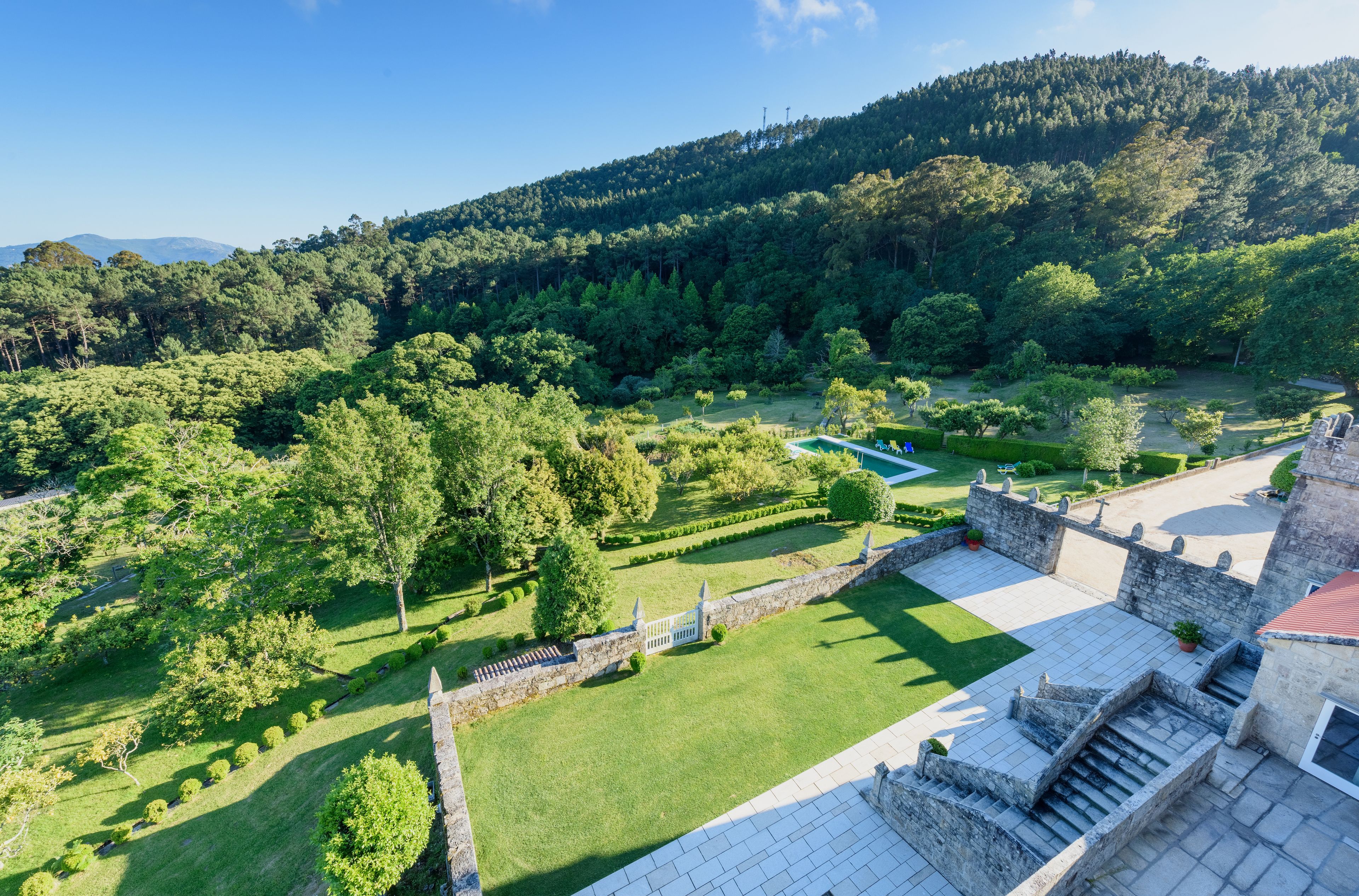 A castle with a well-maintained garden, stone walls, and a clear view of the surrounding forested hills.