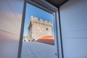 Une vue à travers l’encadrement d’une porte d’un bâtiment en pierre, dont le toit est recouvert de tuiles.