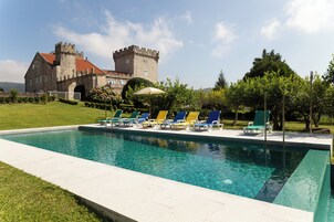 Una piscina con sillas de descanso y un edificio con aspecto de castillo al fondo.