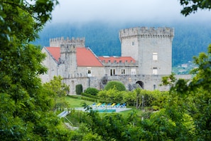 Un château avec un toit recouvert de tuiles rouges, des murs en pierre et une piscine entourée de chaises longues.