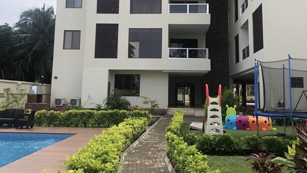 Un edificio residencial de varios pisos con balcones, piscina y zona de juegos para niños.