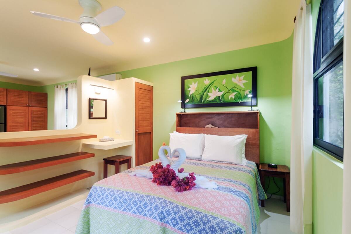 A hotel room with a bed, a vanity, a ceiling fan, and a window.