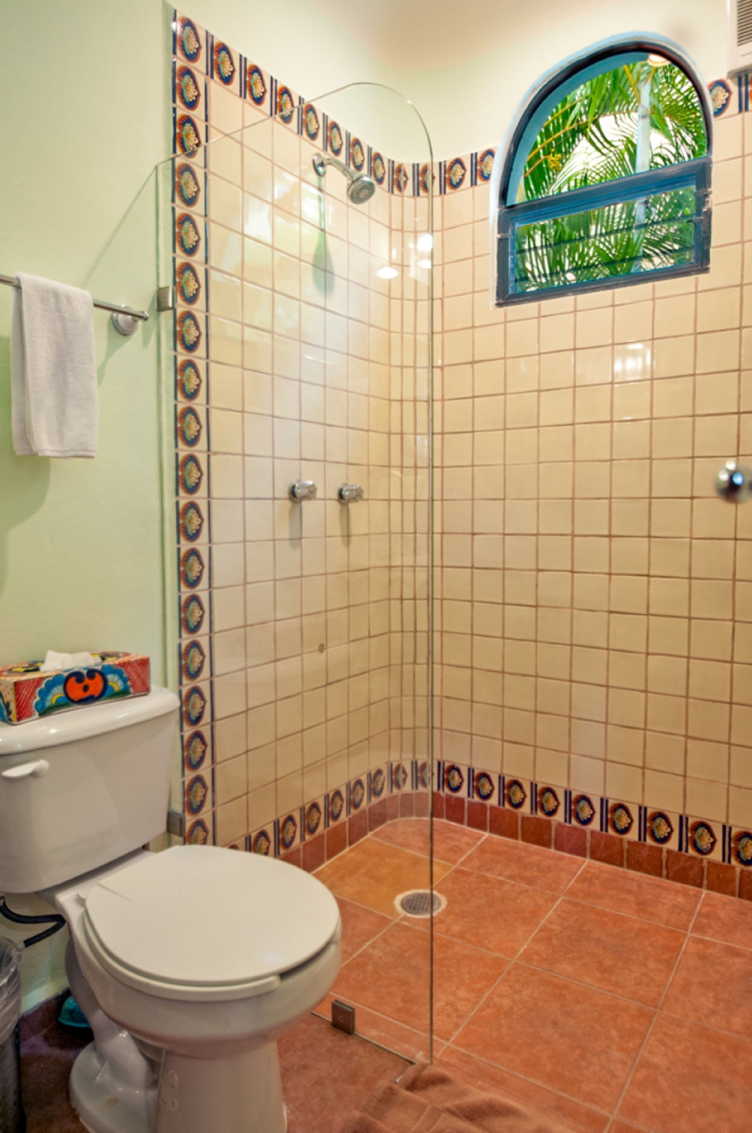 Ein Badezimmer mit Dusche, Toilette und einem Fenster mit Blick auf Palmen.