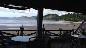 Un área de estar al aire libre con mesas y sillas con vistas a la playa.