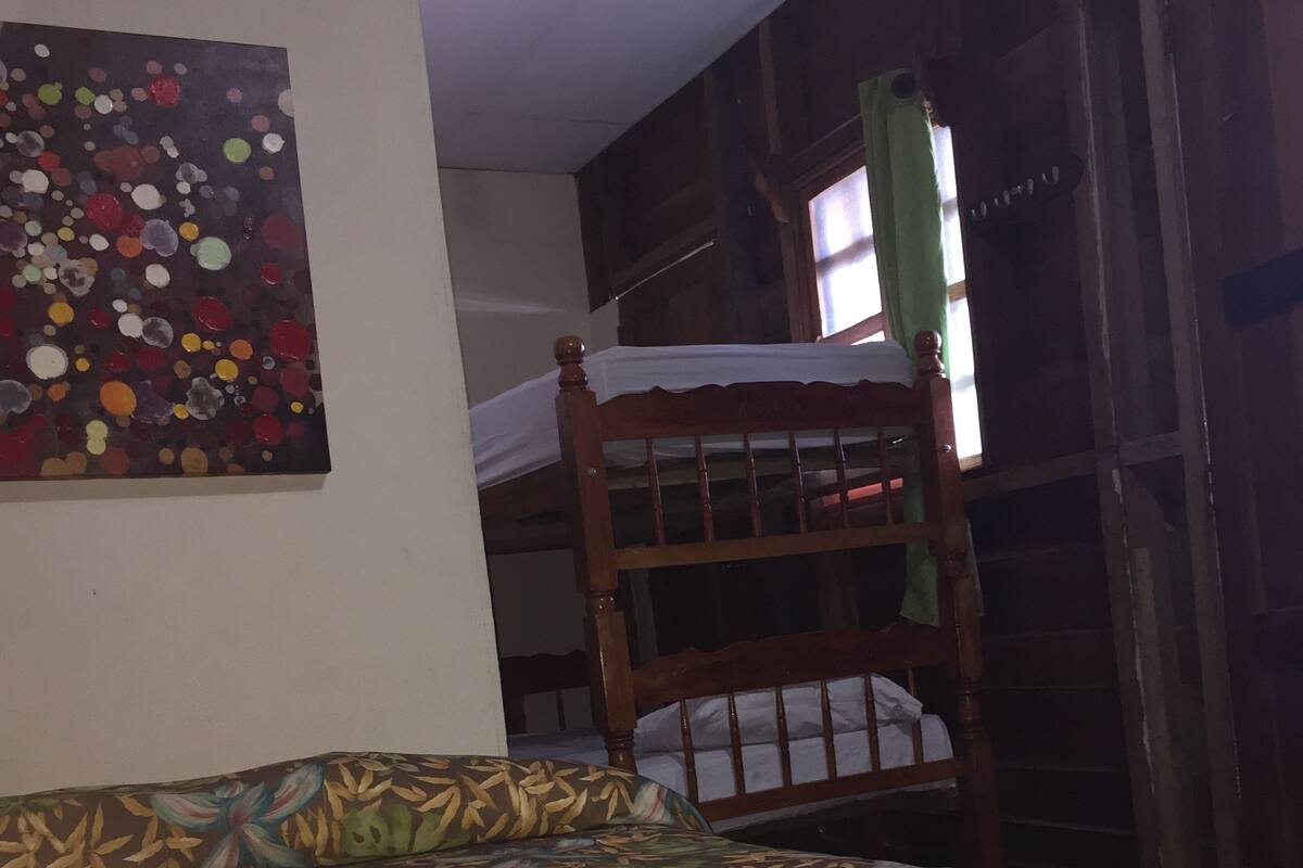 A room with a bed featuring a floral-patterned bedspread, a wooden bunk bed, and a wall with a colorful abstract painting.