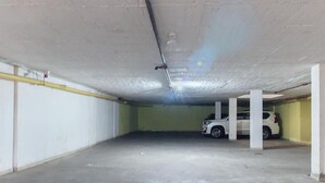 Un estacionamiento subterráneo con pilares de concreto, un coche blanco estacionado en uno de los espacios y un tubo amarillo visible a la izquierda.