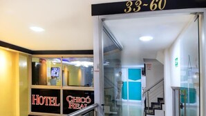 Entrada de hotel con puerta de cristal, una escalera y un cartel que indica los números de habitación 33 a 60.