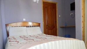 Una cama con cabecera de madera, ropa de cama blanca y una colcha estampada.
