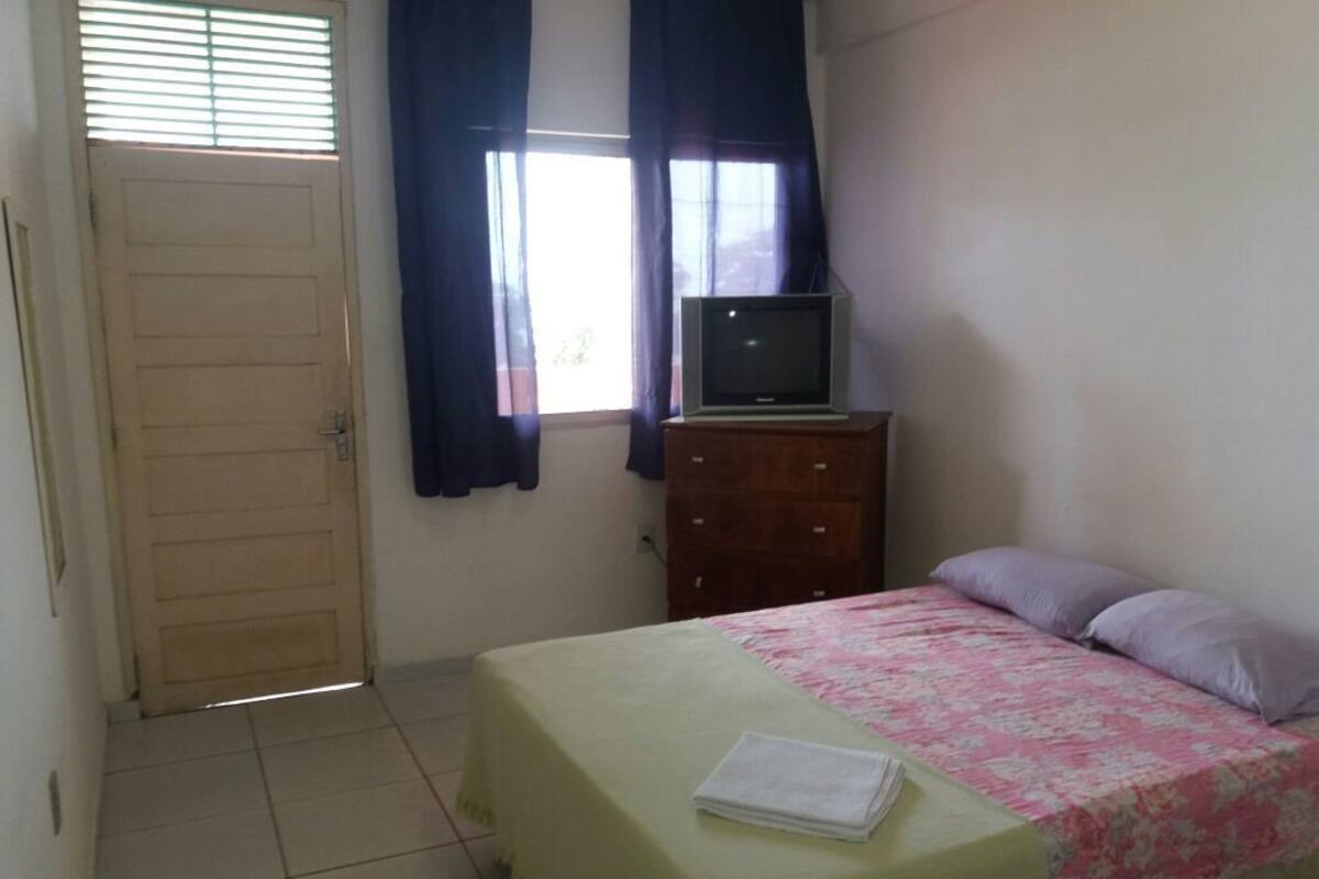A bedroom with a bed, a dresser, a television on top of the dresser, and a door with a window.