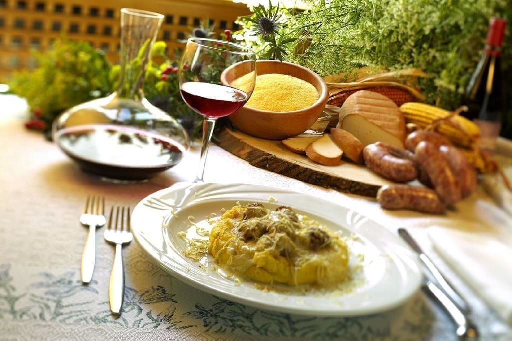 A table set with a plate of food, a glass of red wine, a bowl of yellow powder, and various meats and vegetables.