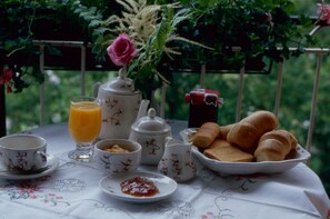 A table set with breakfast items including bread, butter, jam, and tea, with a floral tablecloth and a rose in a vase. - Albergo Miramonti (Arta Terme)