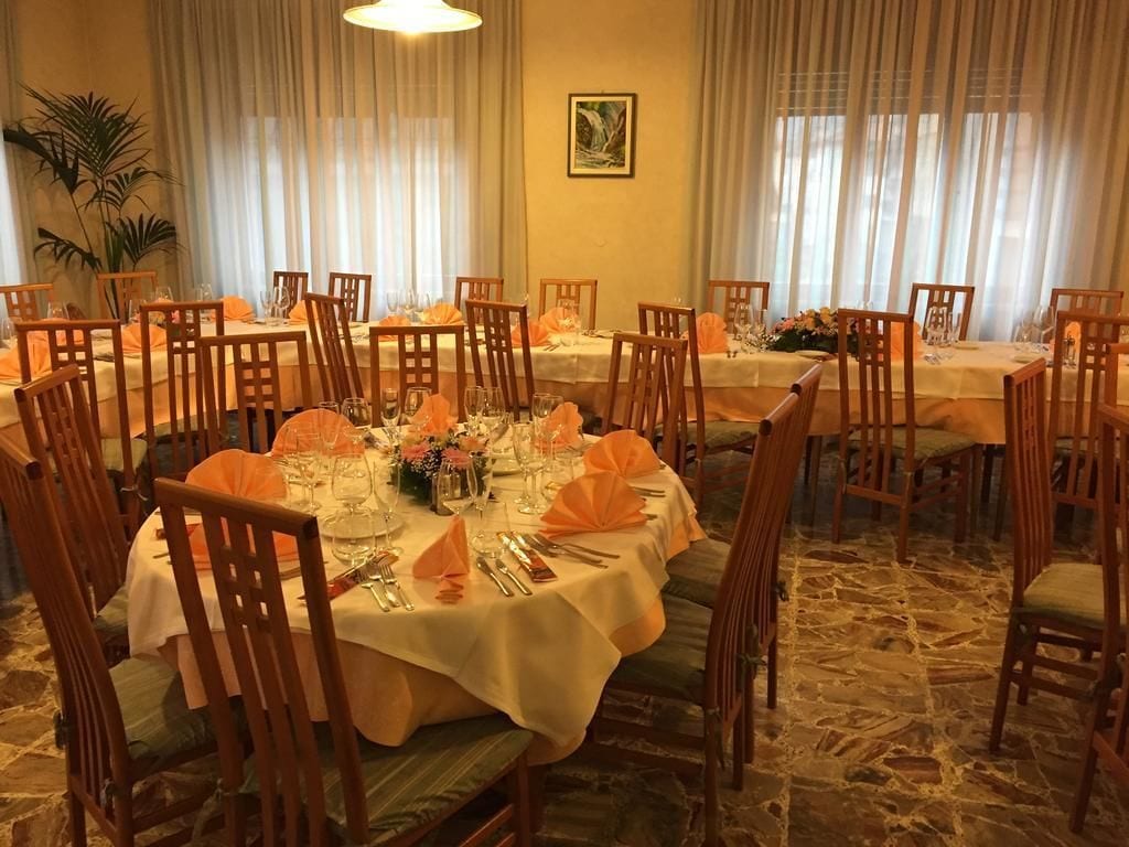 A dining area with round tables set for a meal, surrounded by wooden chairs.