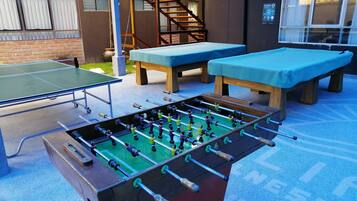 Un espacio recreativo al aire libre con mesa de fútbol de mesa, mesa de ping pong y dos bancos.