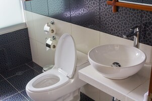 A bathroom with a white toilet, a white sink with a bowl, and a patterned wall.