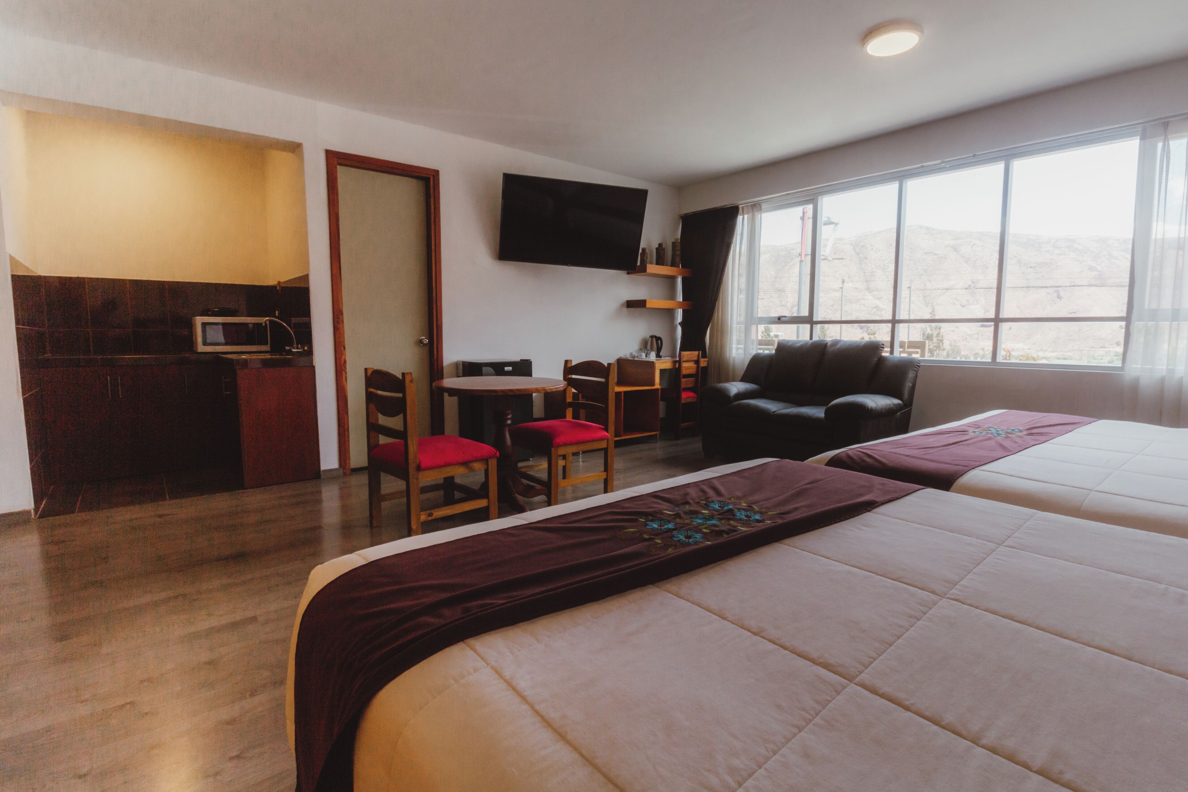 A hotel room with a bed, a desk with a chair, a couch, a TV, and a window with a view.