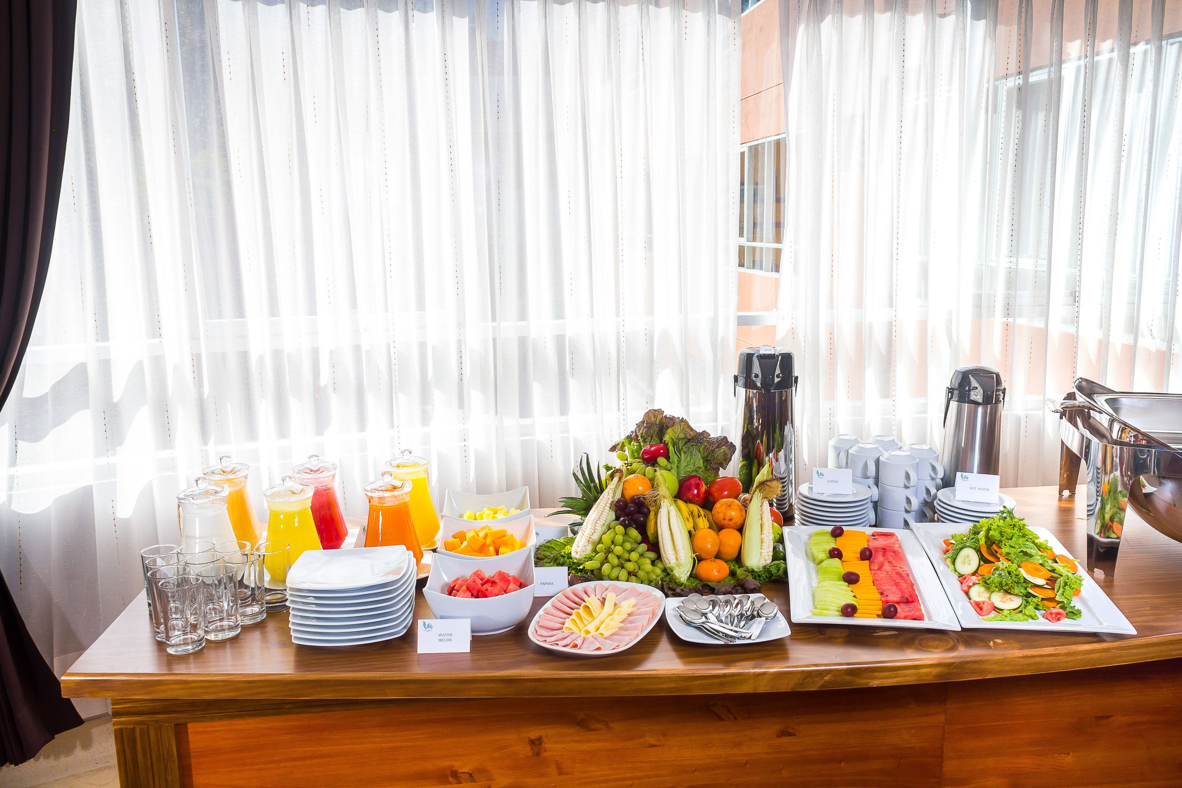 A buffet table with various food items and beverages, including fruits, vegetables, and plates of food.