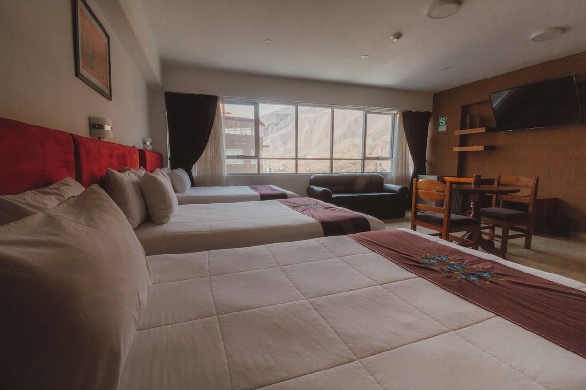 Een hotelkamer met twee bedden, een televisie, een raam met gordijnen en uitzicht op bergen.