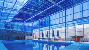 Una piscina interior con paredes de vidrio transparente, paredes de piedra y sillones de descanso.