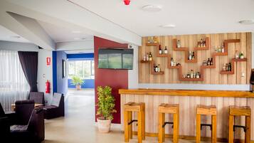 Un área de bar moderna con taburetes de madera, un televisor montado en la pared y una variedad de botellas exhibidas en estantes.