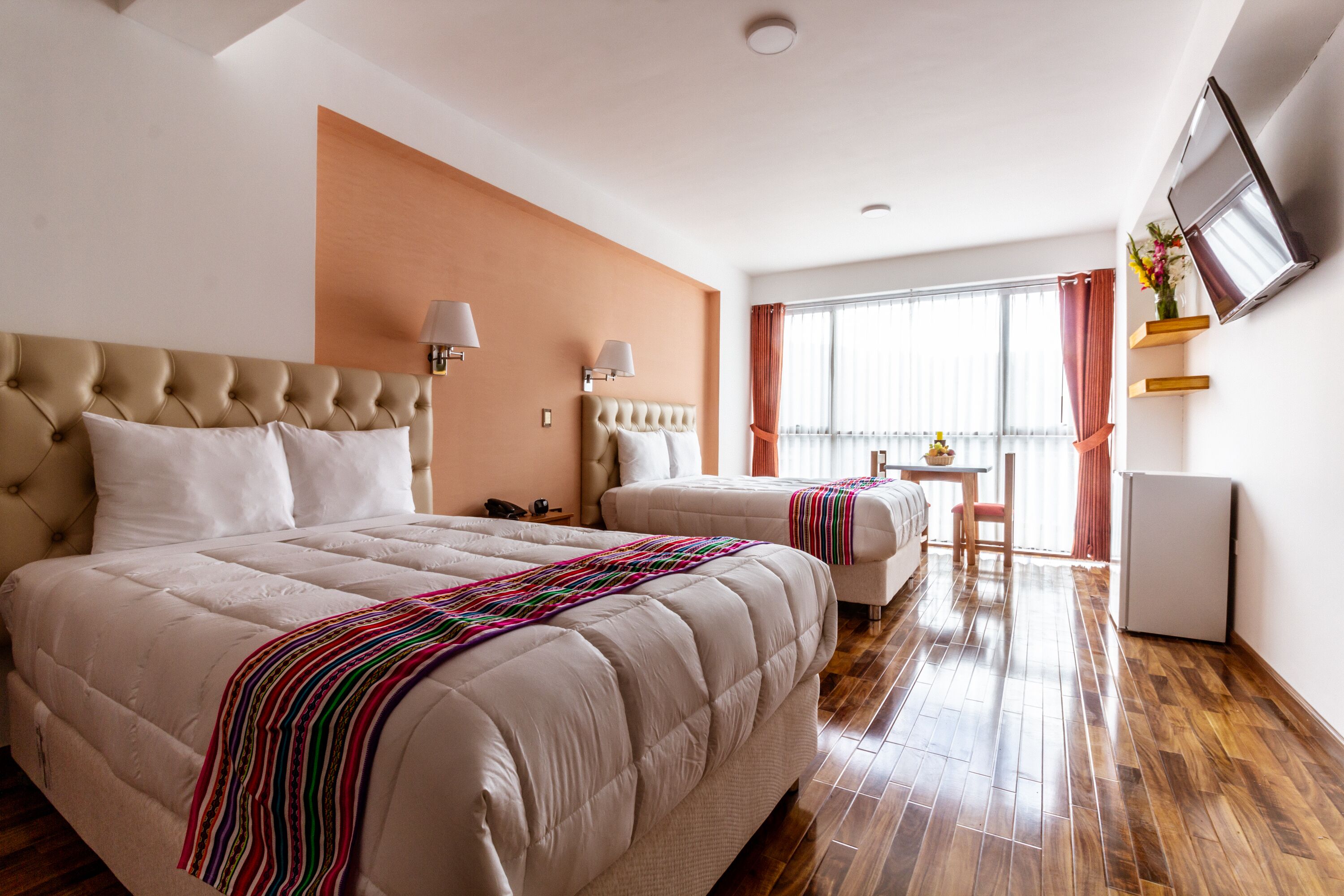 A hotel room with two beds, a TV, a desk, and a window with curtains.
