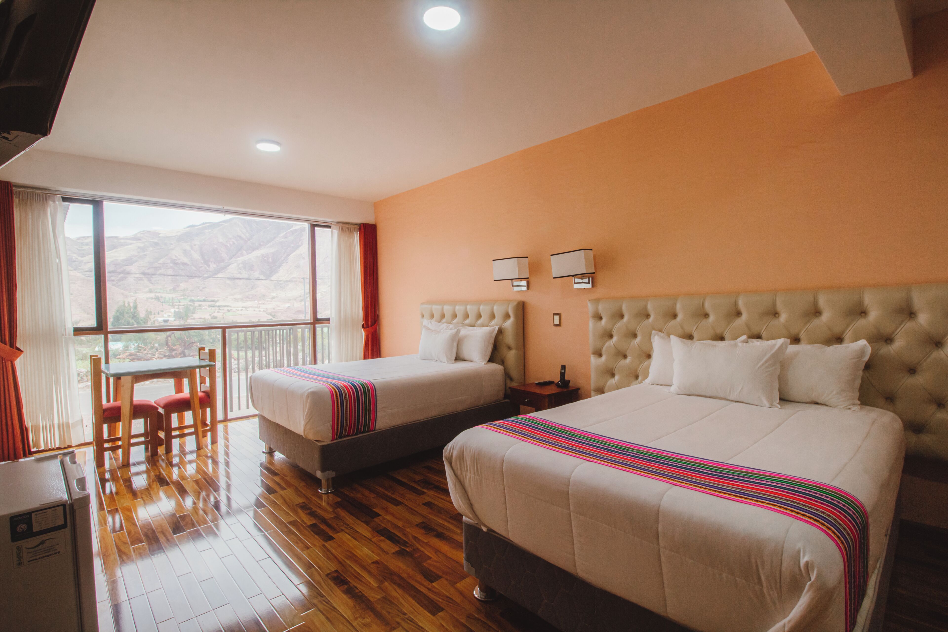 A hotel room with two beds, a balcony, a table with chairs, and a view of the mountains.