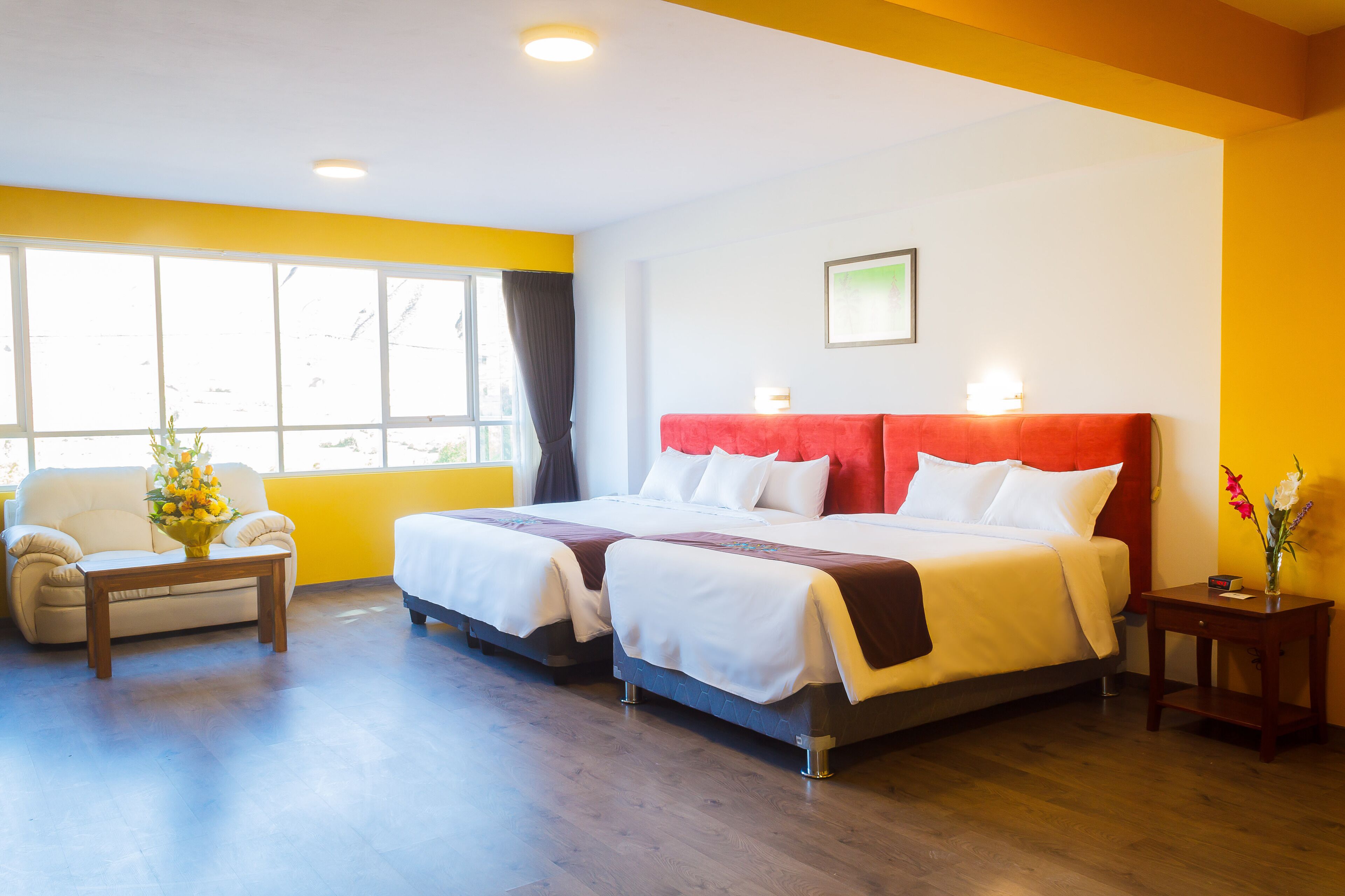 A hotel room with two beds, a sofa, a small table, and a window with curtains.