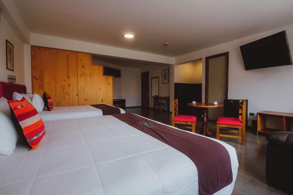 Een hotelkamer met een groot bed, een houten garderobe, een aan de muur bevestigde televisie en een klein tafeltje met stoelen.