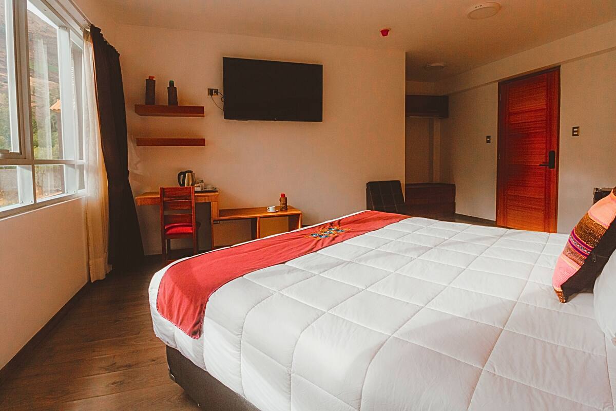 Een hotelkamer met een bed, een bureau, een stoel, een televisie aan de muur en een deur.