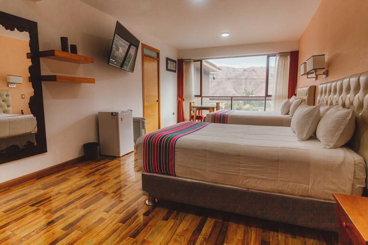 Een hotelkamer met een groot bed, een klein tafeltje, een televisie en een raam met uitzicht op de bergen.