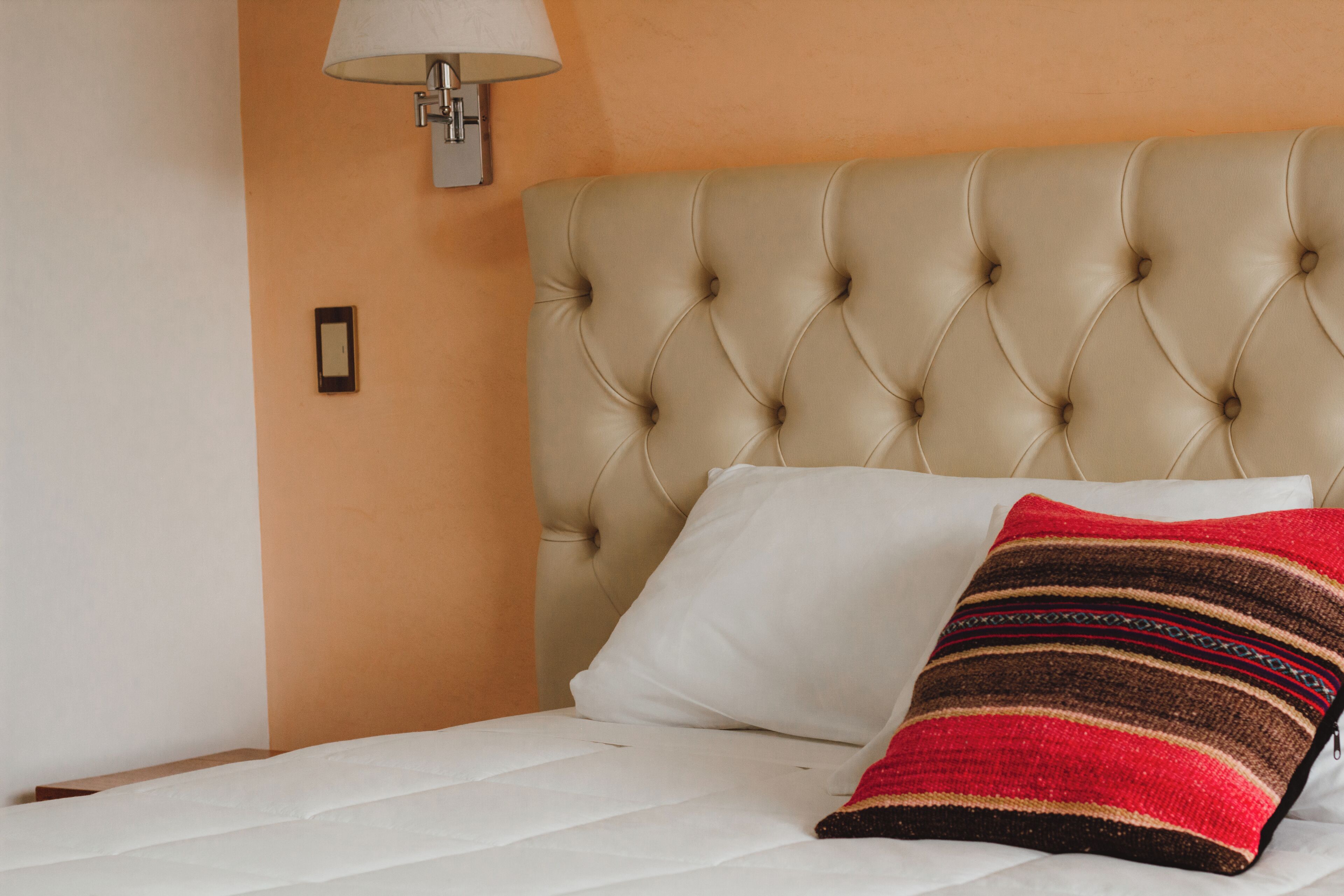 A bed with a tufted headboard, a white pillow, and a striped throw pillow.