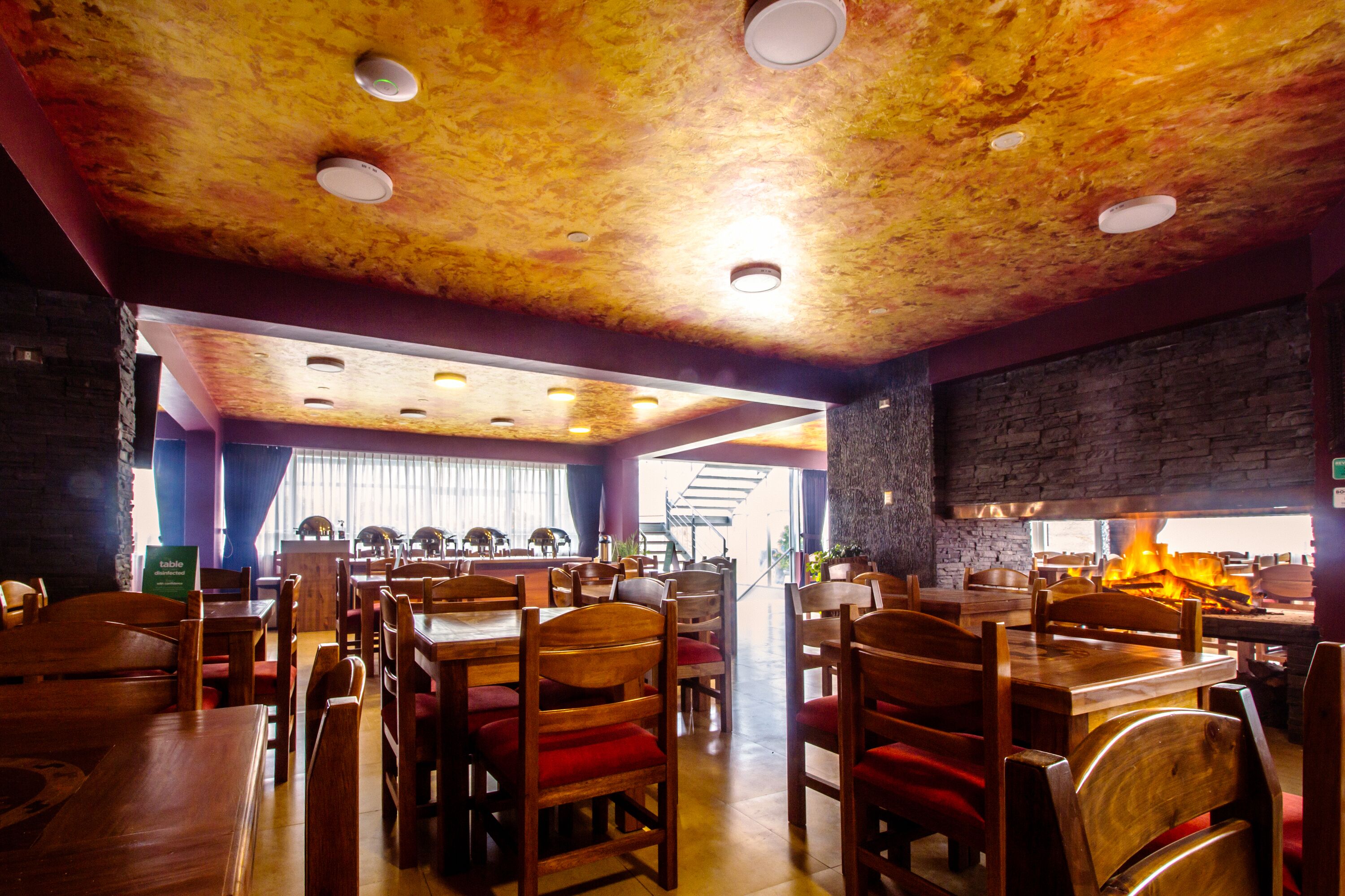 Een restaurantinterieur met houten tafels en stoelen, een stenen muur en een open haard.