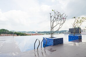 An outdoor pool area with metal railings, a tiled floor, and a view of a cityscape in the background.